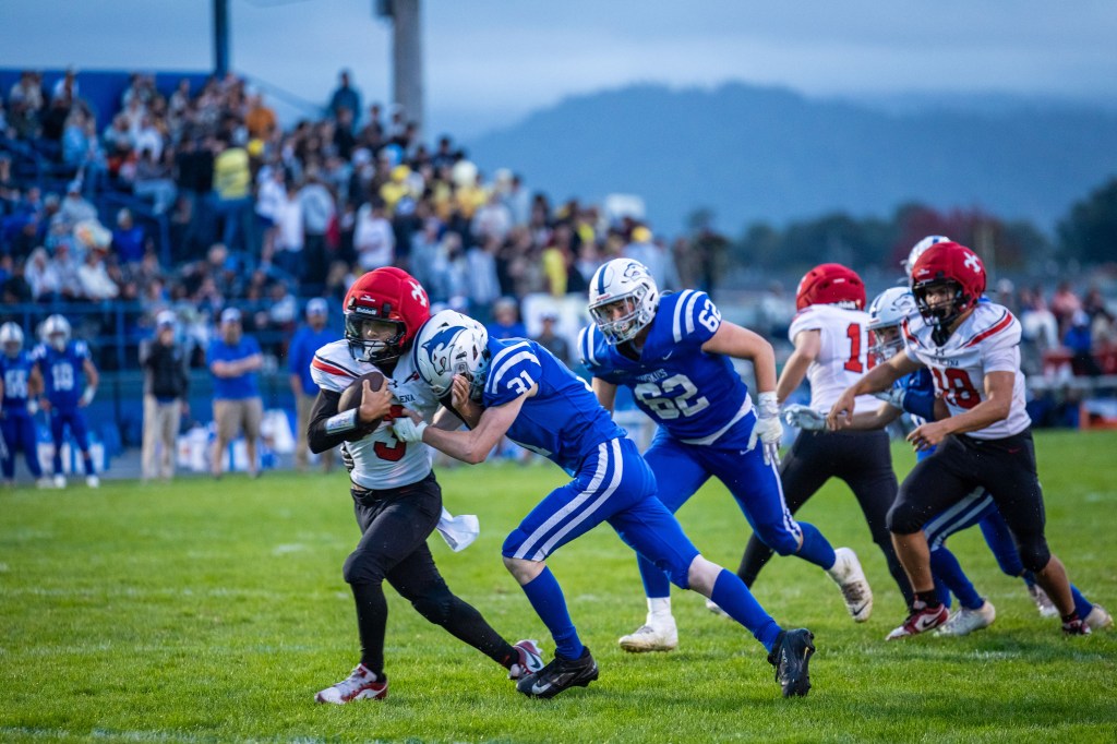 A high school football game in action, featuring players in blue and red uniforms on a green field, with a crowd in the background.