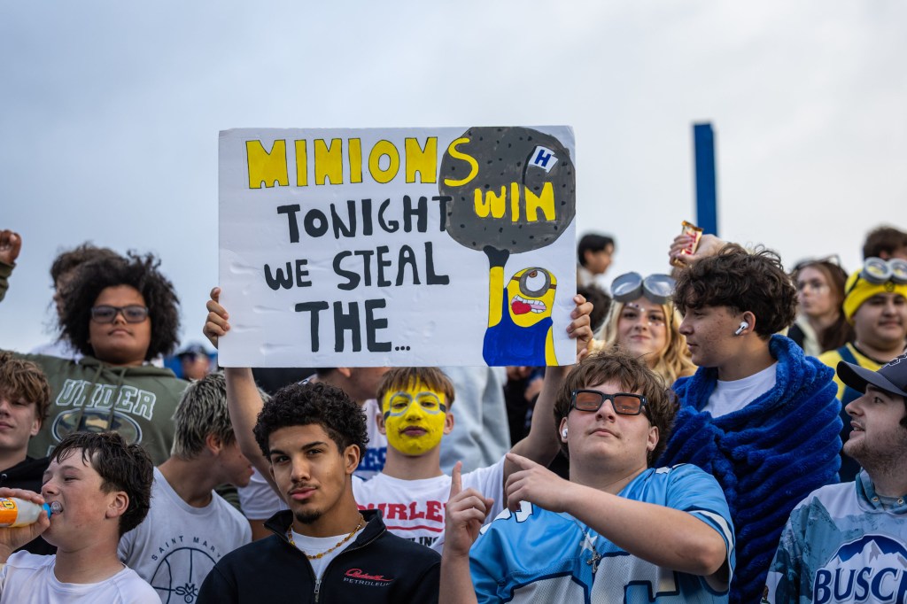 A crowd of enthusiastic fans at a sporting event, with one person holding a sign that reads 'MINIONS WIN TONIGHT WE STEAL THE...' featuring a drawing of a Minion character.