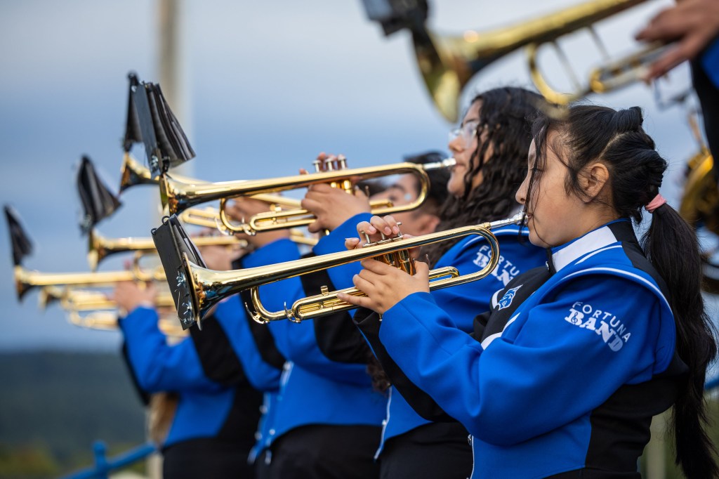 A group of young musicians in blue uniforms playing trumpets at an outdoor event.