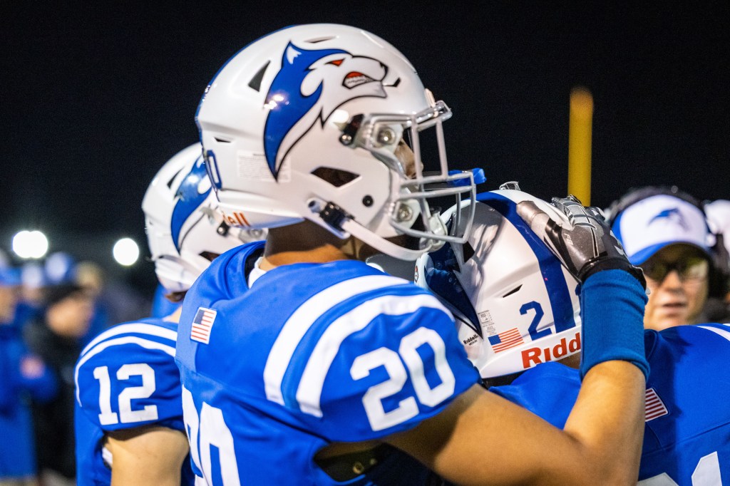 Football players in blue uniforms and helmets celebrating together on the sideline during a night game.