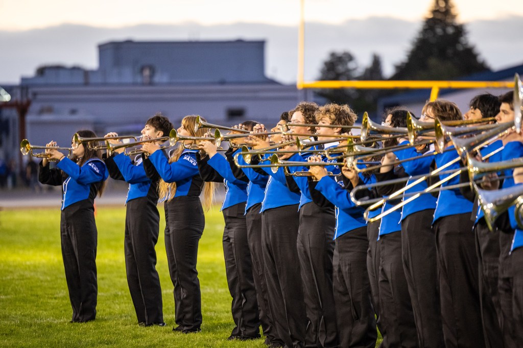 A marching band performing on a grassy field, wearing blue and black uniforms, playing brass instruments.