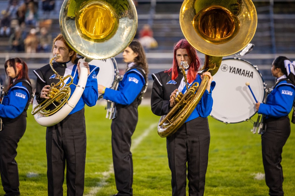 A marching band featuring musicians playing tubas on a football field, dressed in blue and black uniforms.