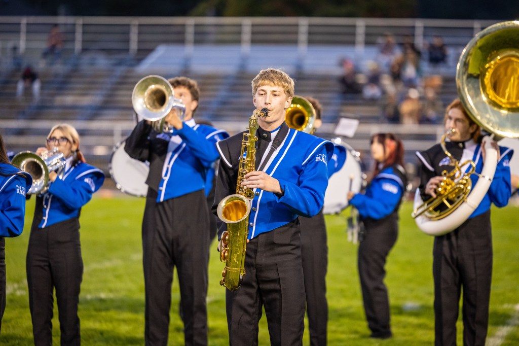 Marching band members playing instruments on a football field during a performance.