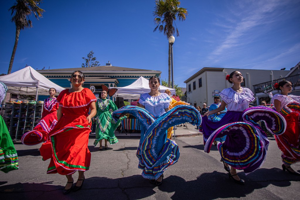 Group of dancers in colorful traditional dresses performing a dance outdoors during a cultural festival.