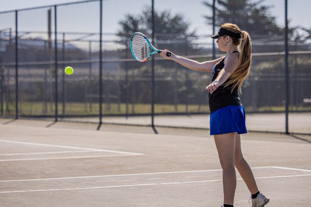 A young woman playing tennis on an outdoor court, preparing to hit a ball with her racket.
