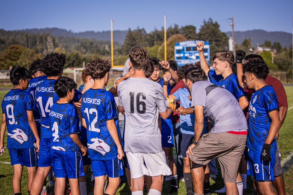 A group of young soccer players in blue uniforms huddled together on a field, celebrating and strategizing before a game.