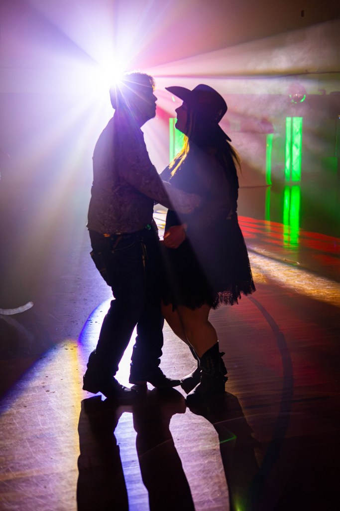 A couple dancing closely under colorful stage lights, creating a romantic atmosphere in a dimly lit space.