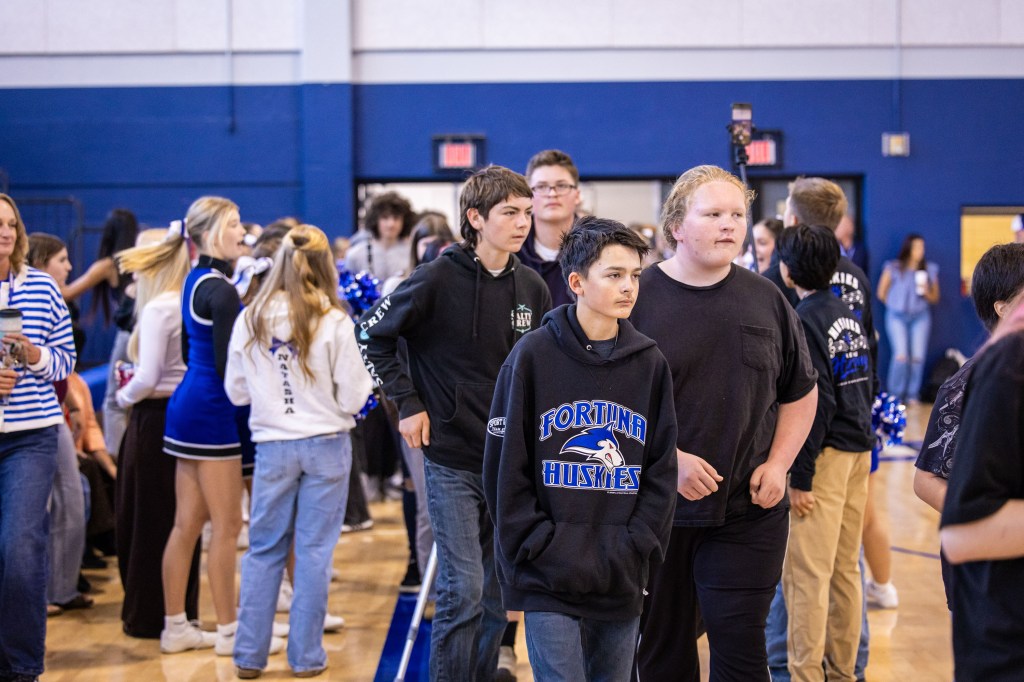 A group of students walking together in a gymnasium during a school event, with cheerleaders and spectators in the background.