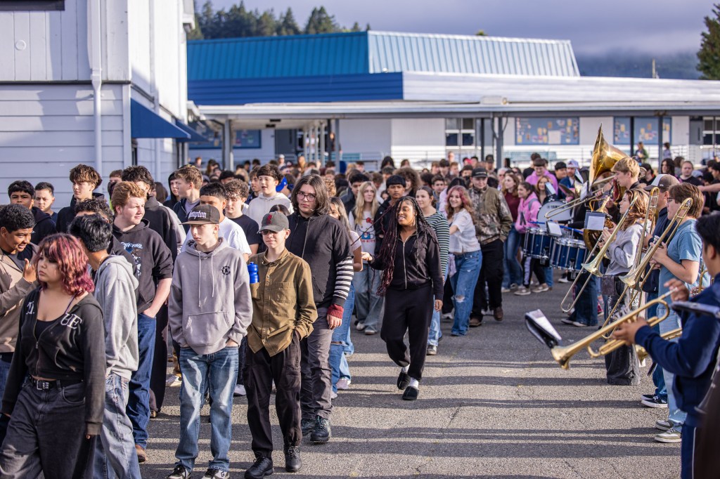 A crowd of students lined up outside a school, with some playing musical instruments in the foreground.