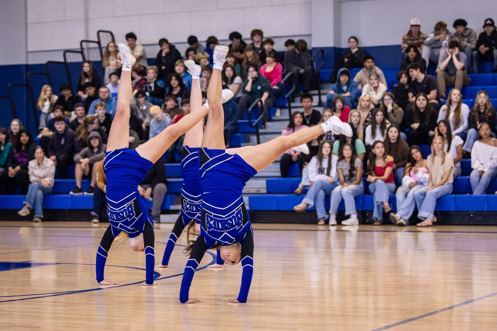 Cheerleaders performing a back handspring in front of an audience at a school event.