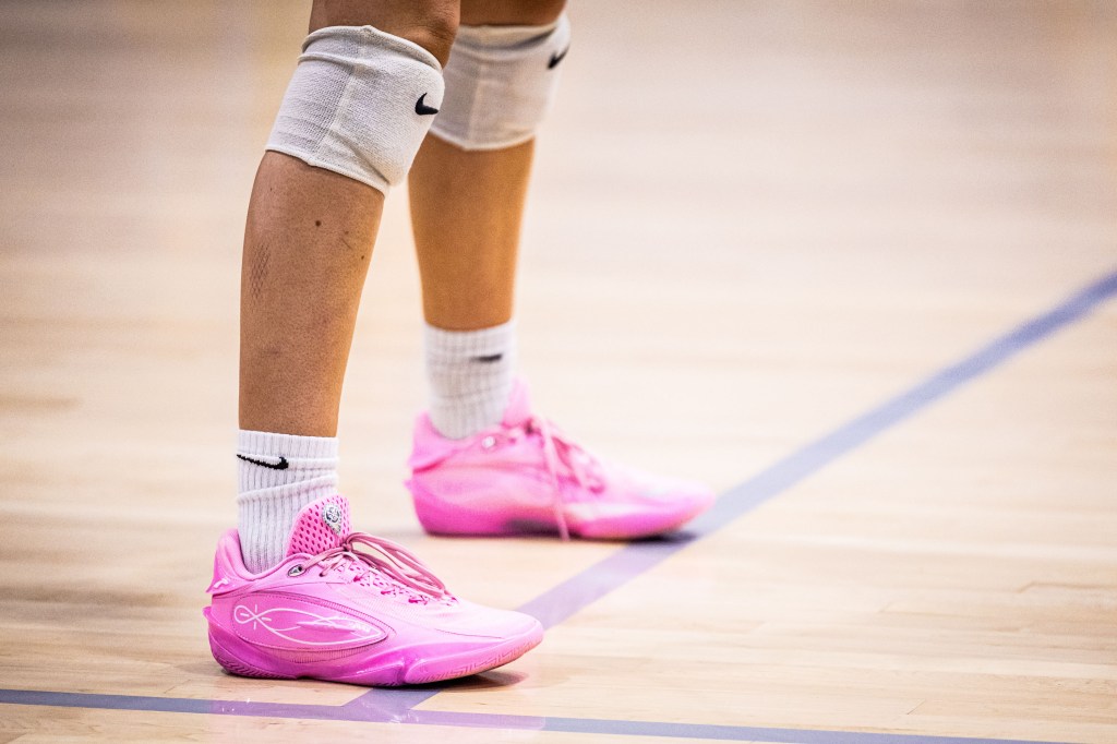Close-up of a person's legs wearing pink athletic shoes and white knee pads on a basketball court.