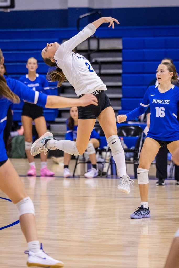 A volleyball player leaps to hit the ball during a match, with teammates and opponents visible in the background.