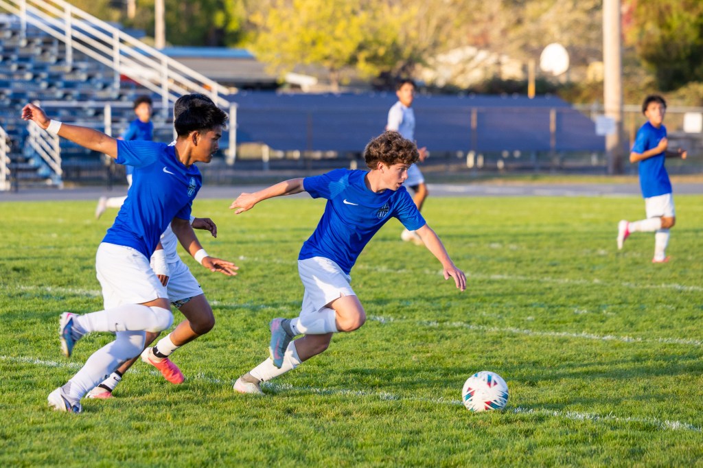A soccer match in progress with players in blue uniforms chasing a ball on a grassy field.