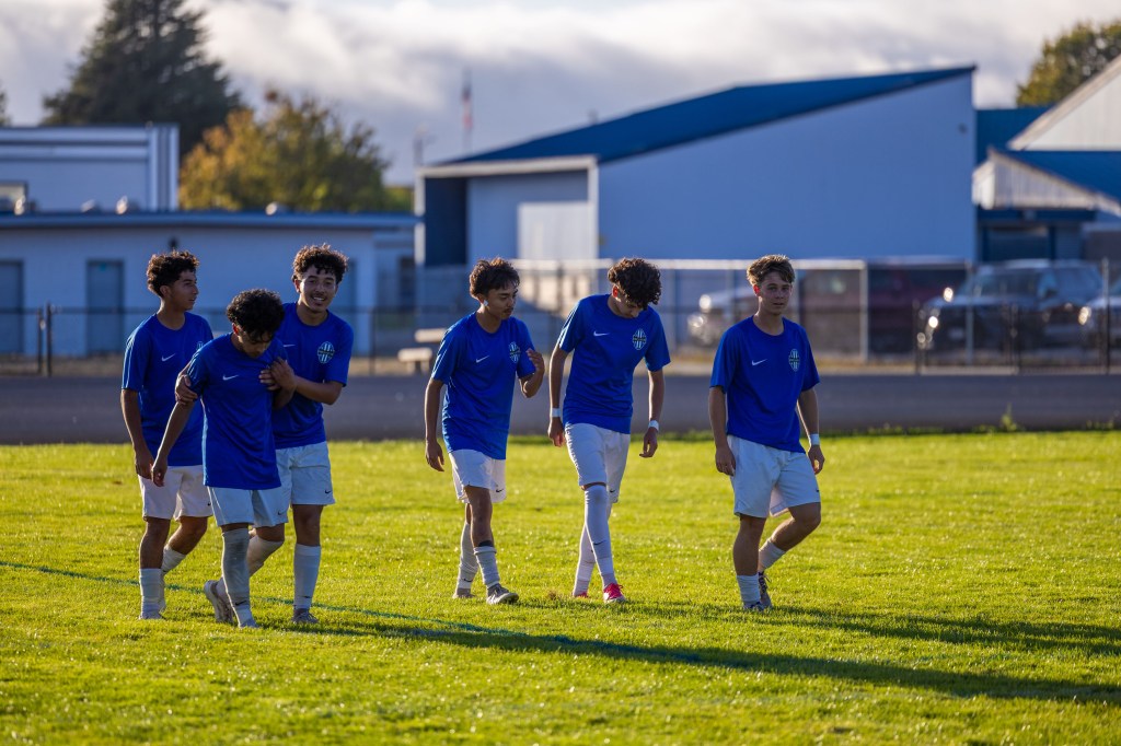 A group of young soccer players in blue jerseys walking across a grassy field, showing camaraderie after a match.