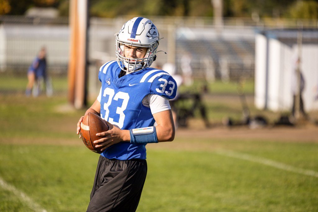 A young football player wearing a blue jersey with the number 33 holds a football in a practice field setting, looking to pass.