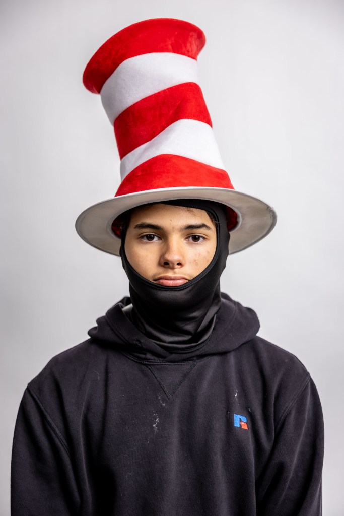 A person wearing a tall red and white striped hat and a black face covering, posing against a plain background.